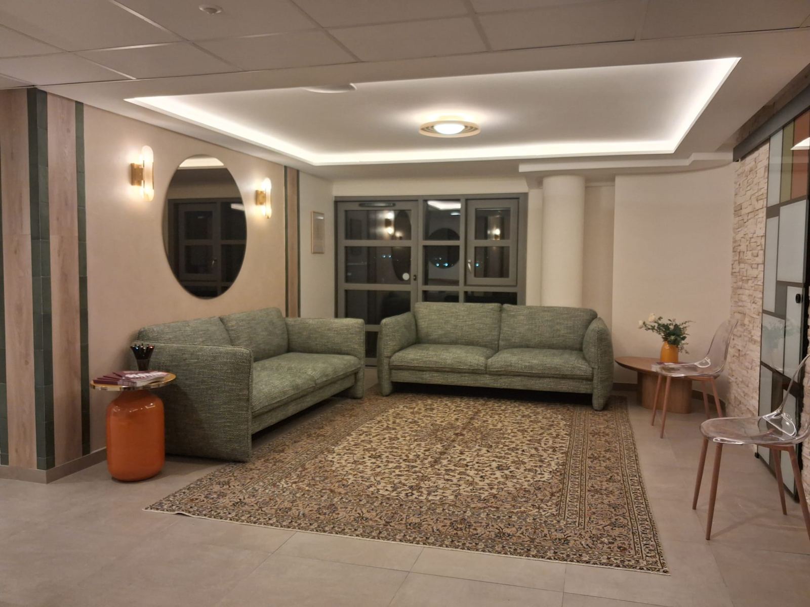 Espace d'accueil : plafond suspendu avec gorge lumineuse, miroir rond, habillage bois et faïence verte
