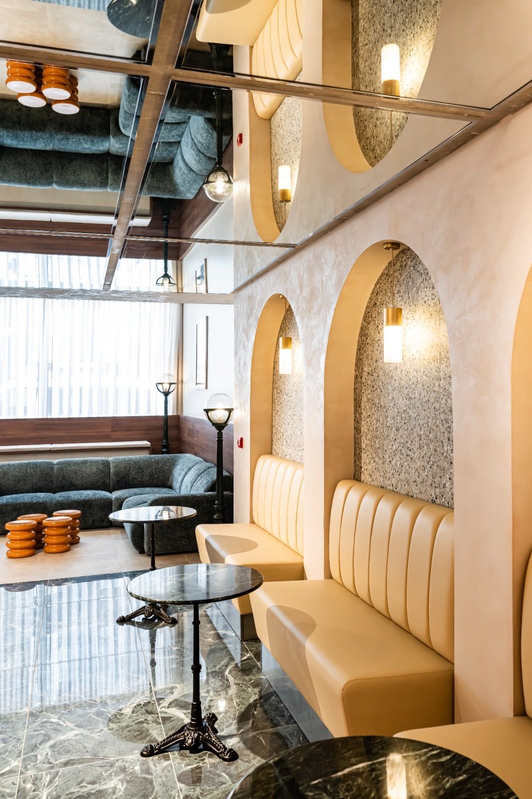 Banquettes capitonnées dans des niches cintrées en terrazzo, suspensions laiton, tables bistrot en marbre