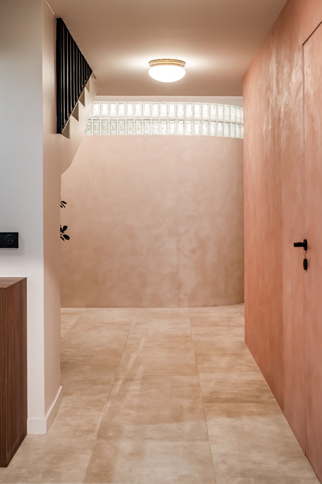 Circulation : enduit décoratif rose, mur courbe et bandeau en briques de verre, porte affleurante